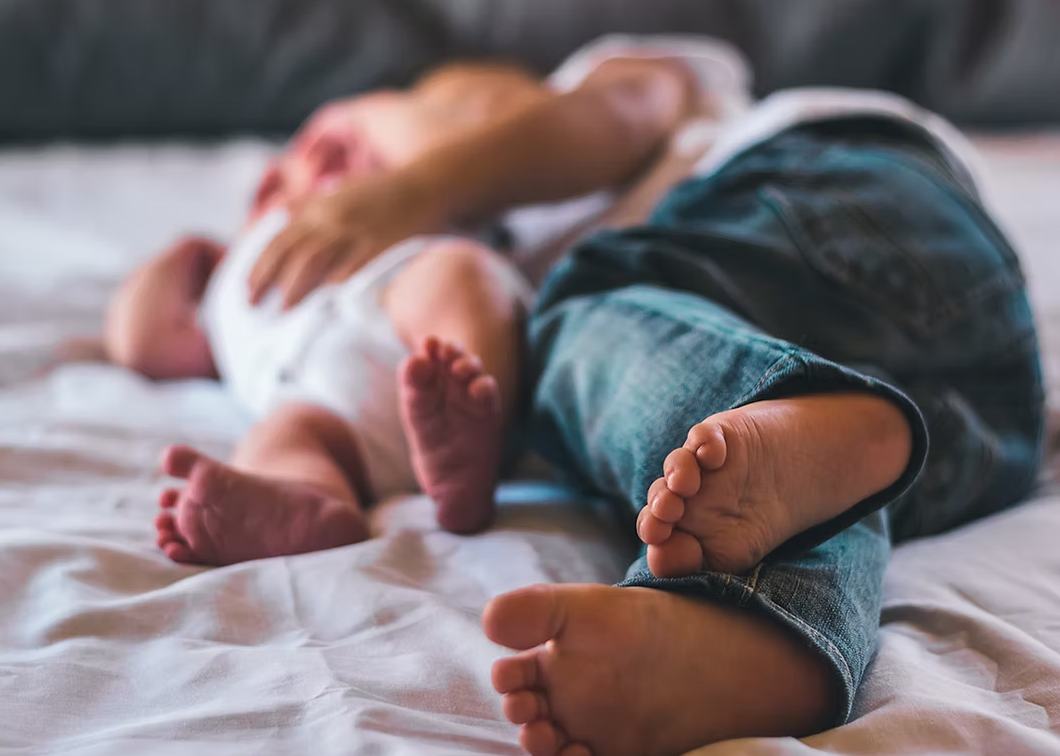 Un parent et son bébé allongés sur un lit, pour illustrer les soins destinés aux enfants